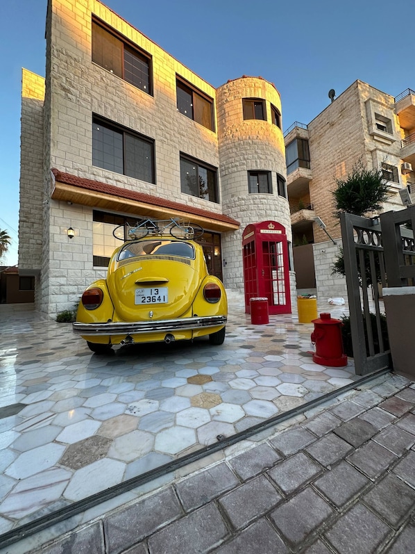 A yellow vintage car parked in front of a building with a stone facade and a red telephone booth.