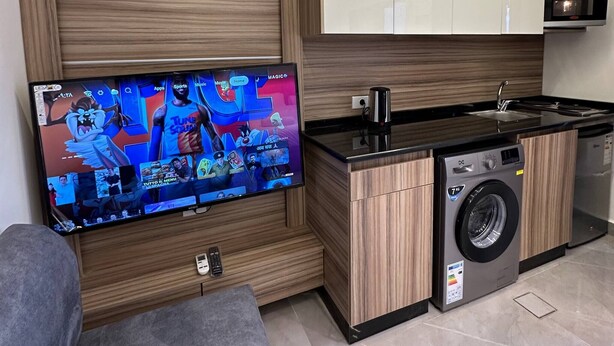 Una cocina moderna con lavadora integrada, un televisor de pantalla plana en la pared y armarios de madera.