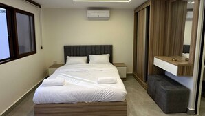 Un dormitorio moderno con una cama grande, mesitas de noche, equipo de aire acondicionado, un banco empotrado y un espejo.