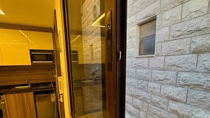 A modern kitchen with built-in appliances, a large window with a view of a stone building, and a door with a keypad lock.