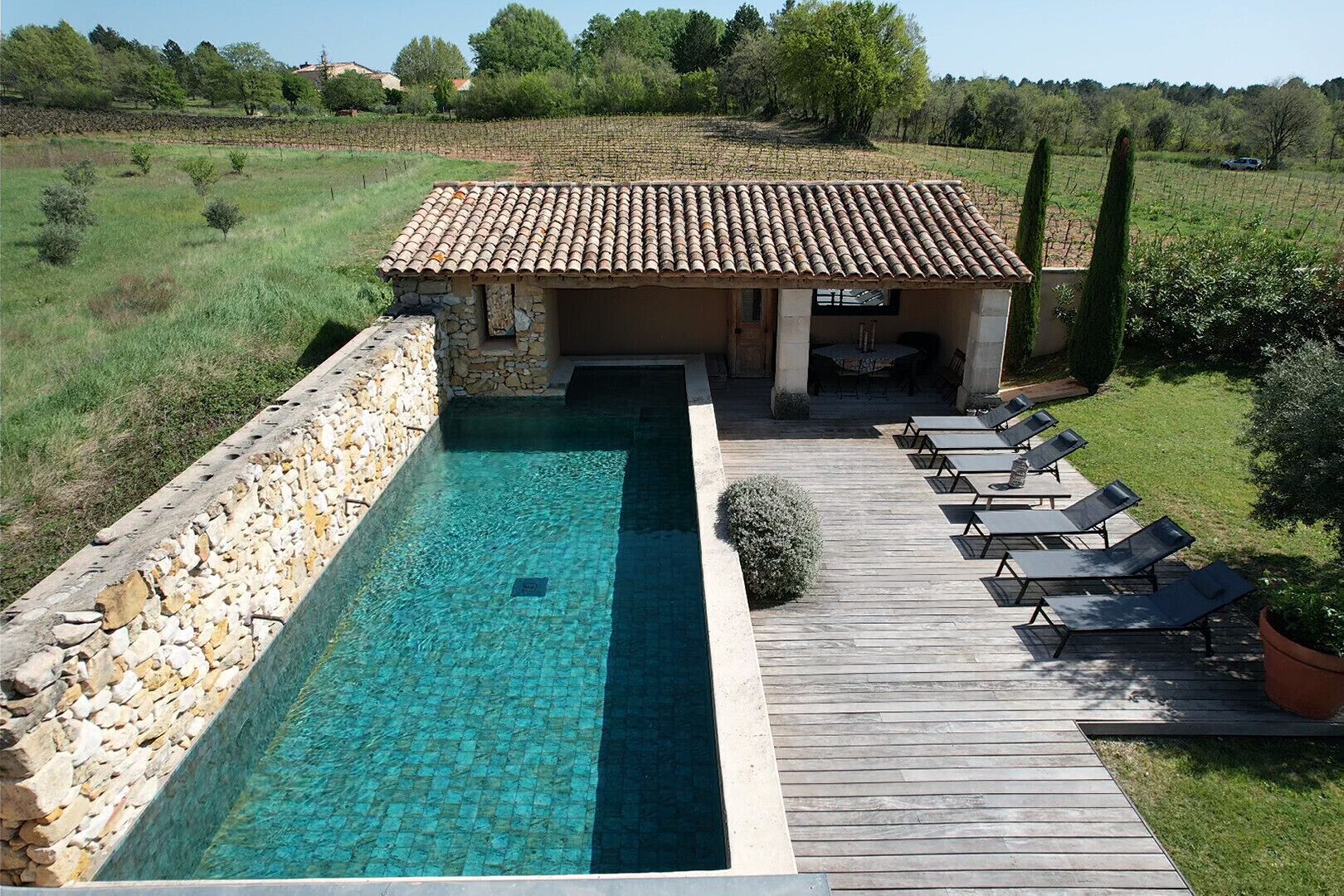 A villa with a swimming pool, a wooden deck, and lounge chairs.