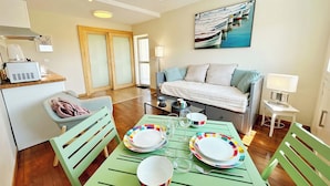 Una sala moderna con una mesa de comedor lista para cuatro personas, un sofá, un cuadro y una kitchenette.