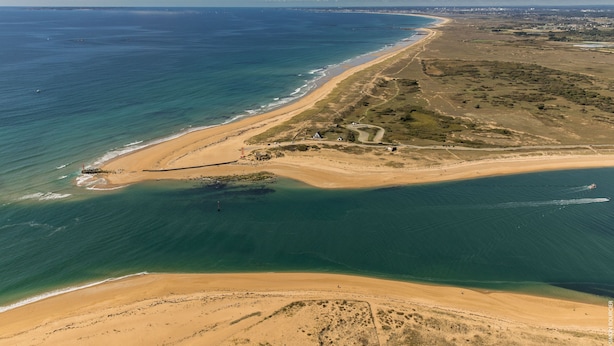 Vista aérea de una zona costera con playa, un pequeño asentamiento y cielo despejado.