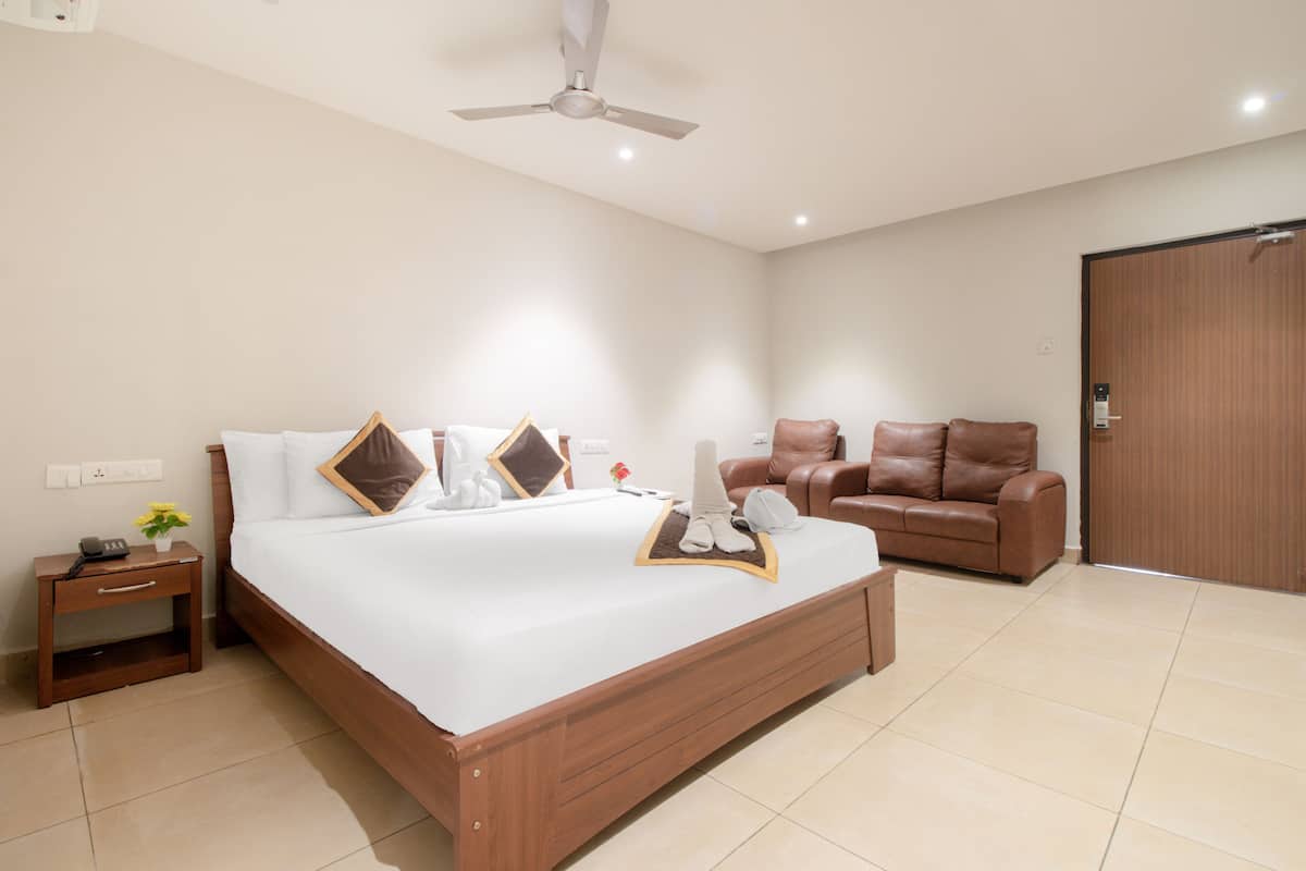 A hotel room with a large bed, a brown leather sofa, a wooden nightstand, and a ceiling fan.