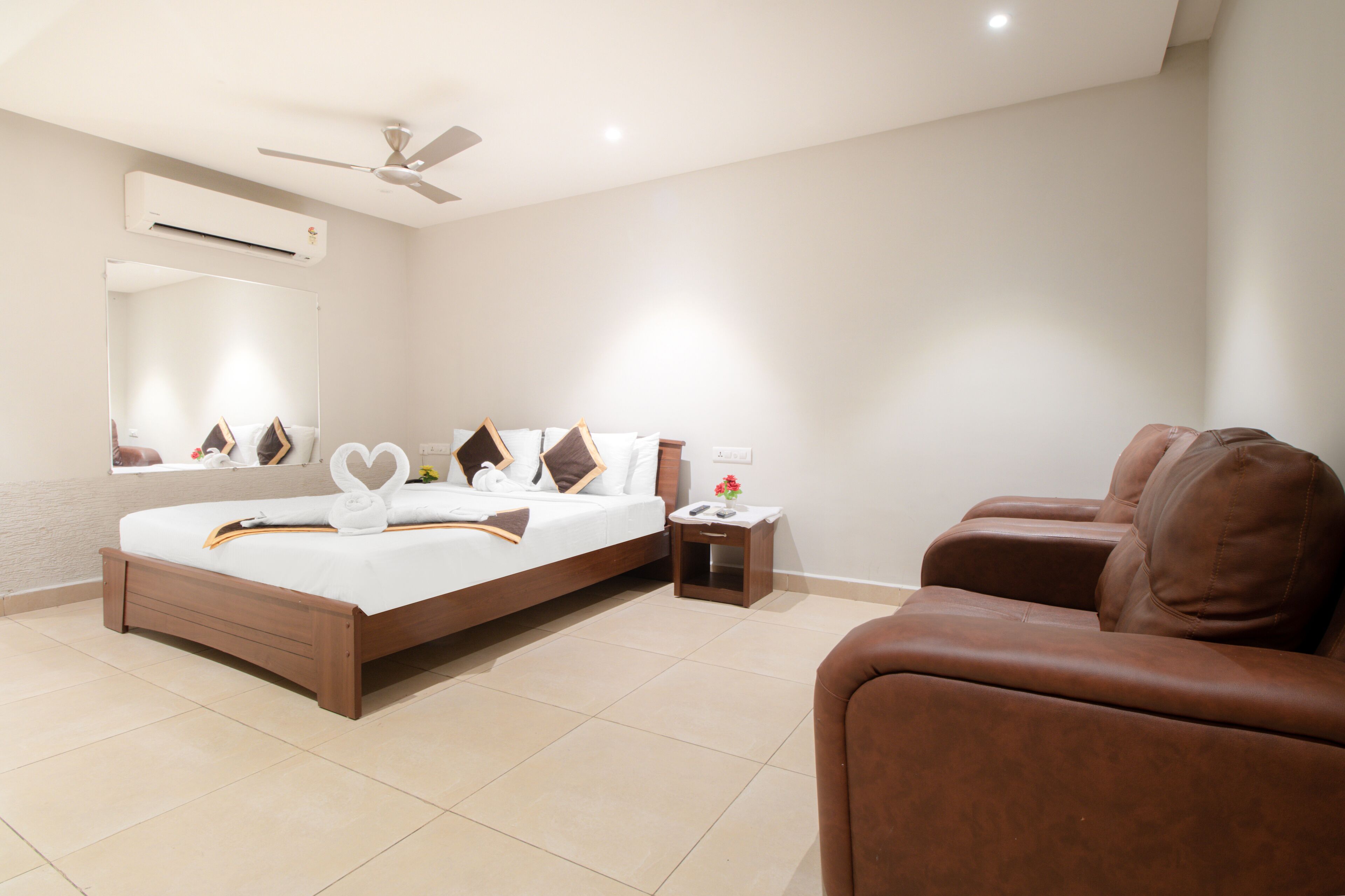 A modern hotel room with a large bed, a small bedside table, a brown leather sofa, and a ceiling fan.