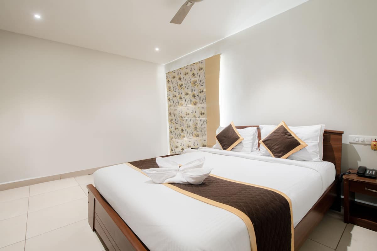 A neatly made bed with a brown headboard, white bedding, and a folded towel on the footboard.