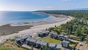 A coastal residential area with modern houses, a beach, and a forested landscape.