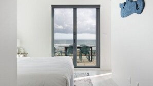 A bedroom with a large sliding glass door leading to a balcony overlooking the ocean.