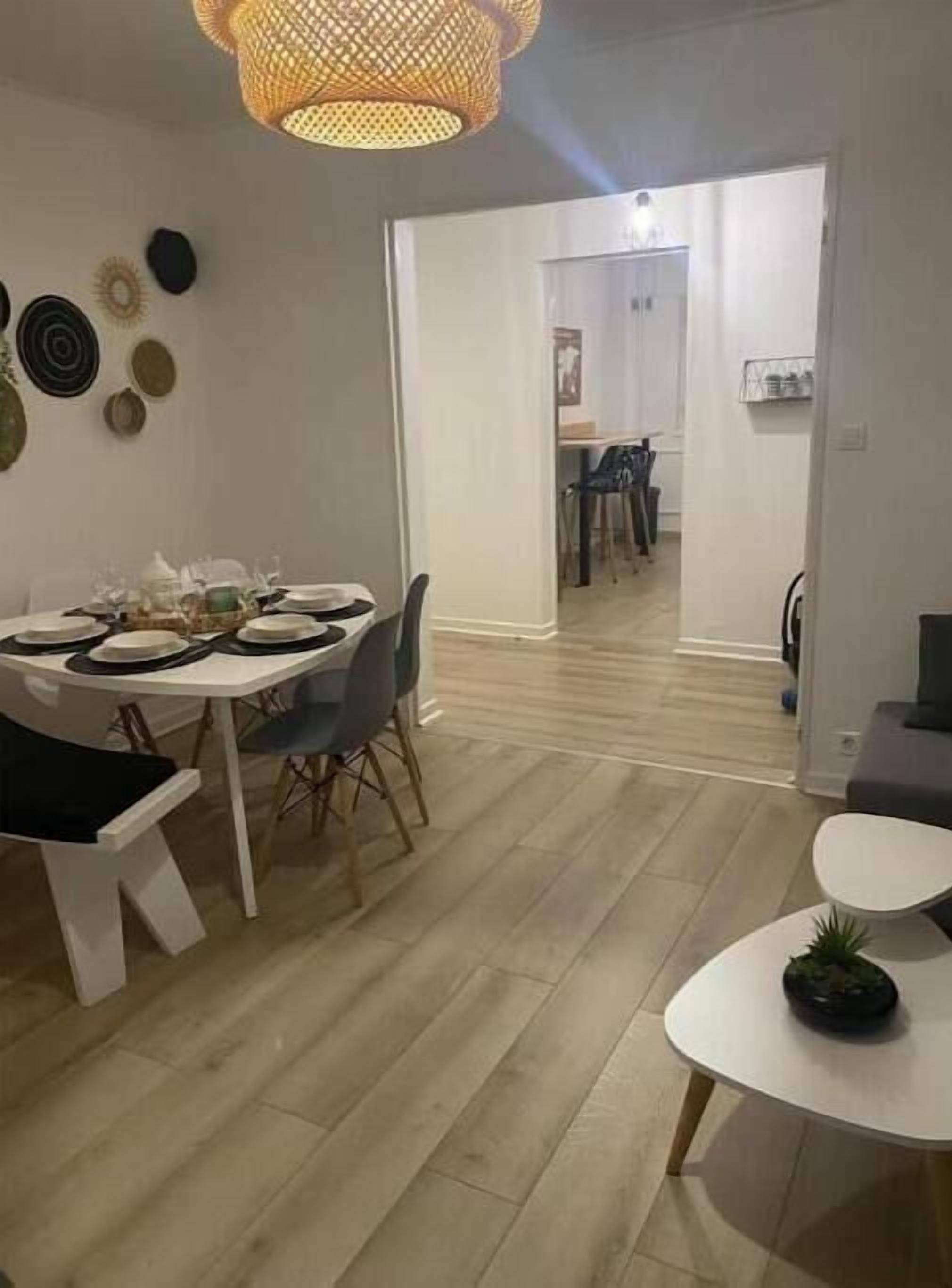 A dining area with a round table set for four, a white chair, and a small table with a plant.