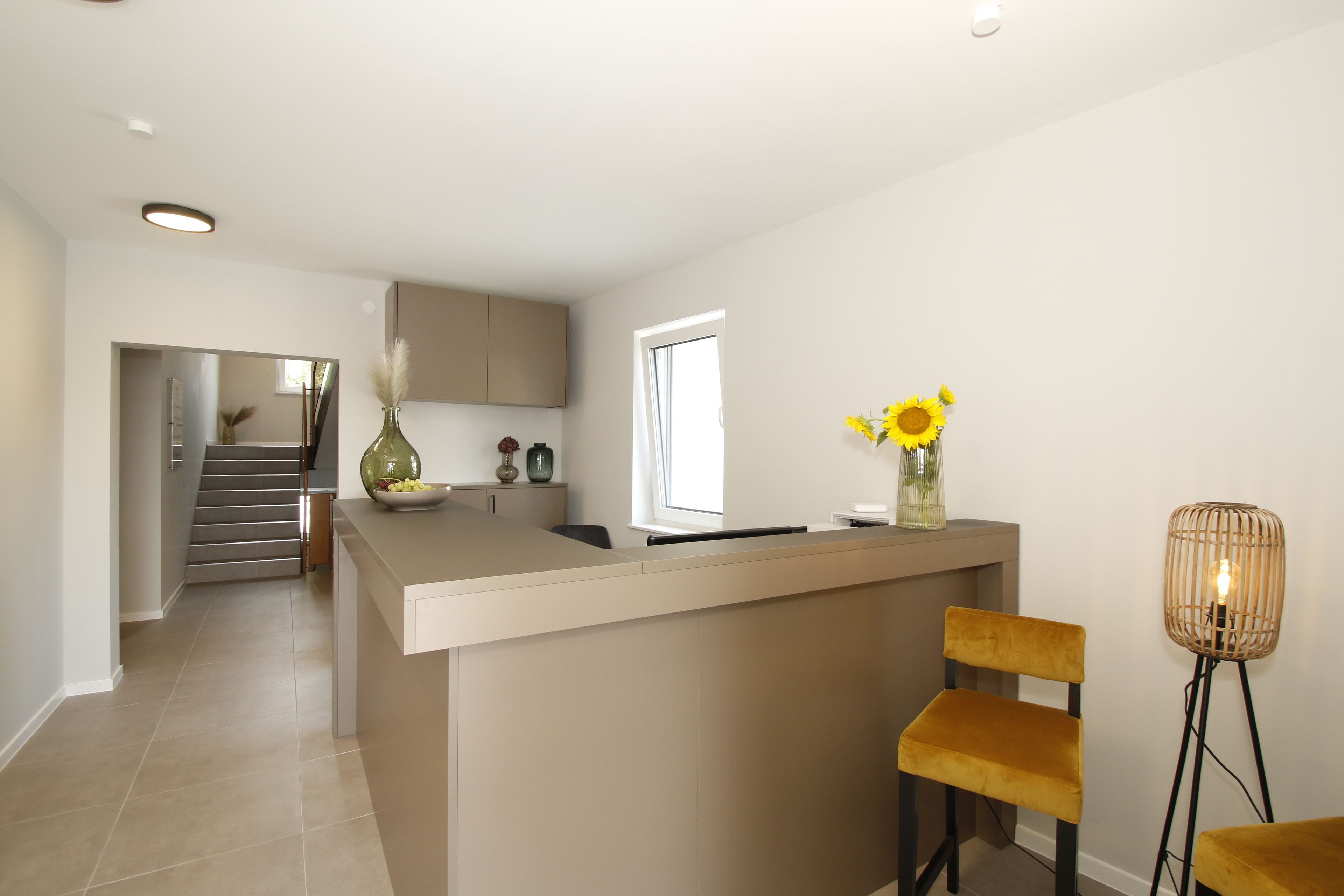 A modern kitchen with a central island, a dining area with two chairs, and a staircase leading to another level.