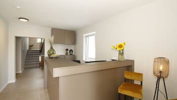 A modern kitchen with a central island, a dining area with two chairs, and a staircase leading to another level.