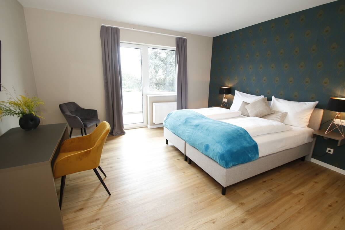Habitación de hotel con cama, escritorio, silla, ventana y lámpara.