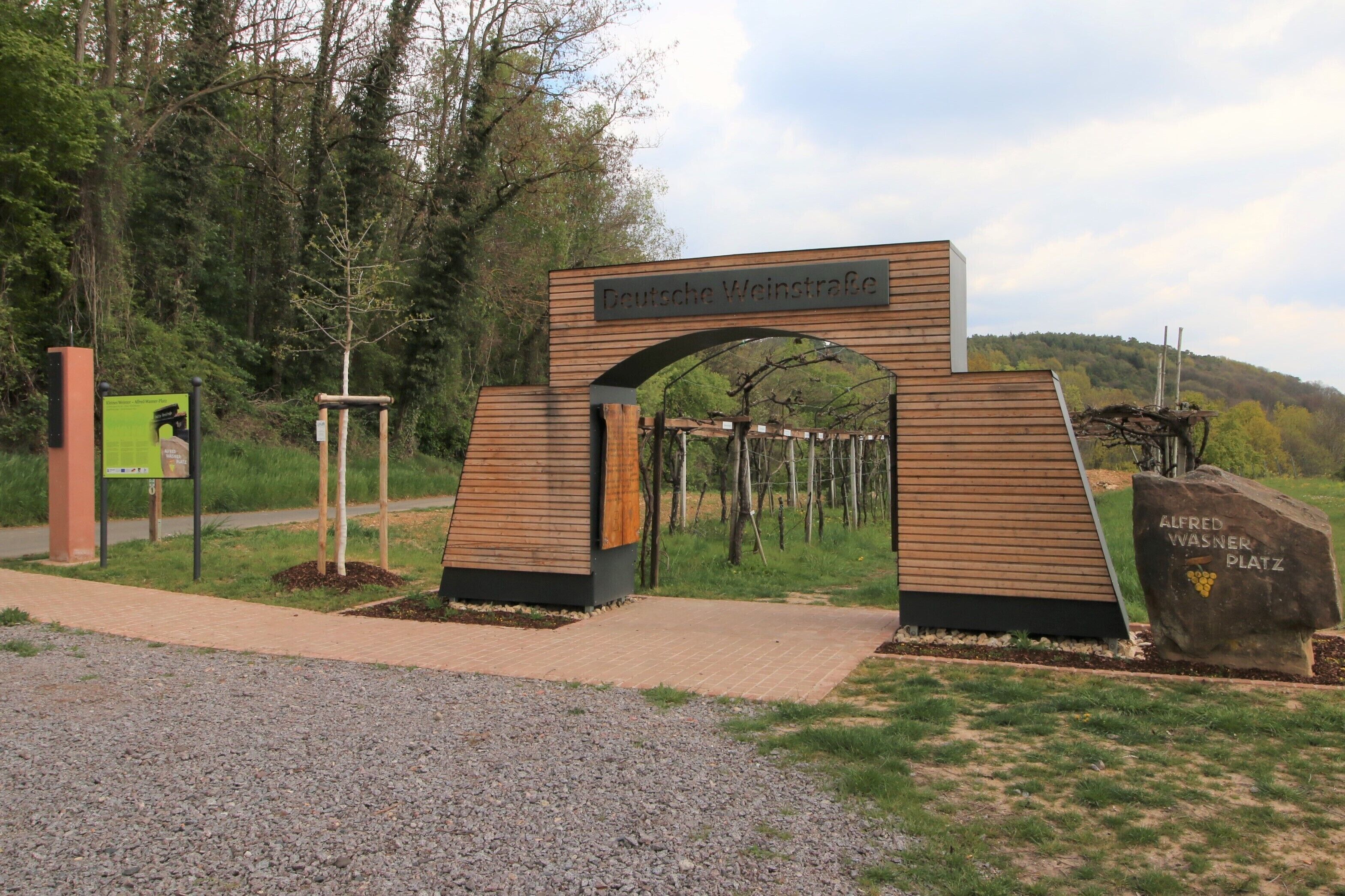 A wooden archway with a sign reading "Deutsche Weinstrasse" and a plaque labeled "Alfred Wasner Platz".