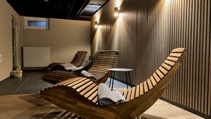 Un área de relajación moderna con tumbonas de madera y una mesita, con techo inclinado y un radiador al fondo.