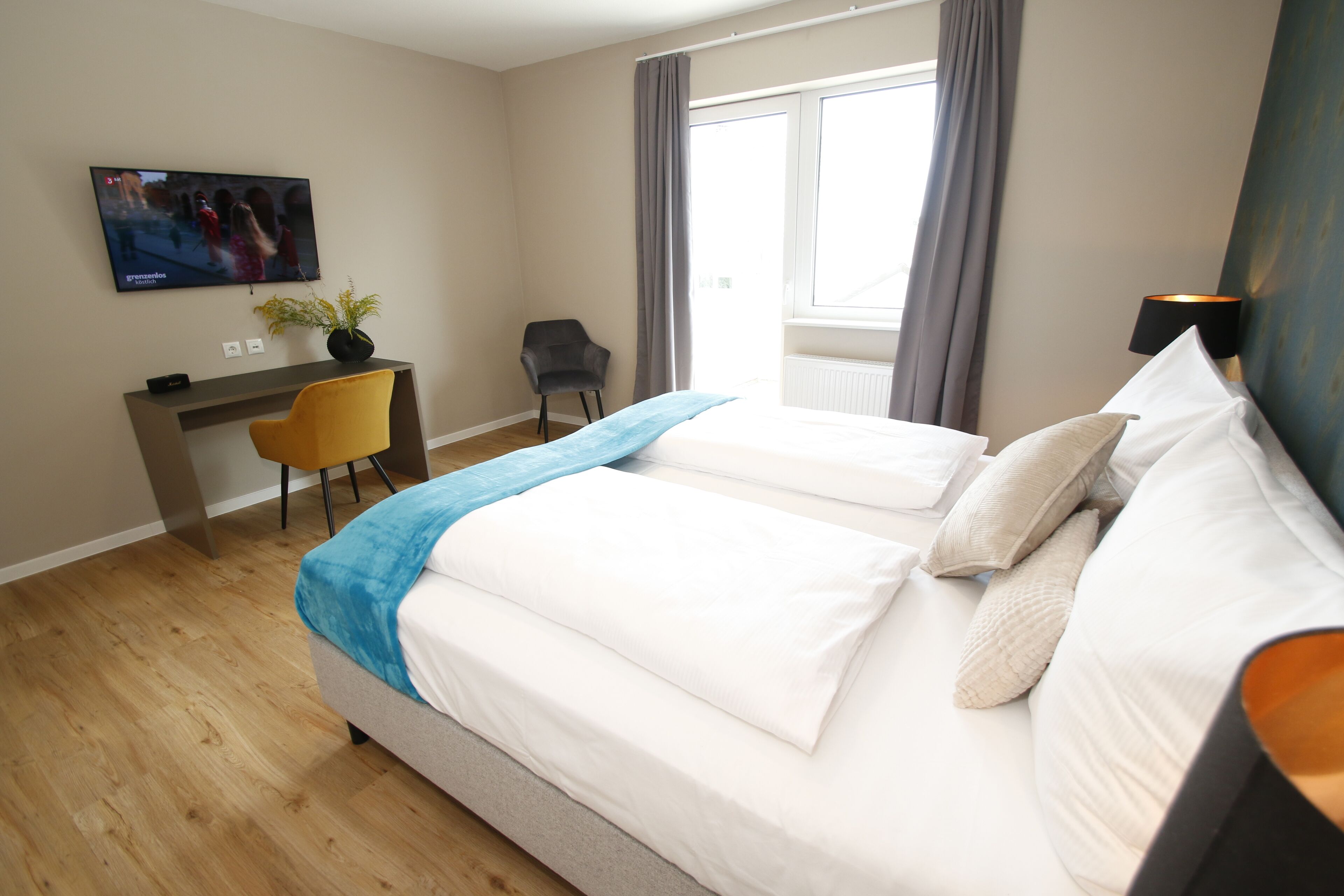 Una habitación de hotel con dos camas, un escritorio con silla, un televisor y una ventana con cortinas.