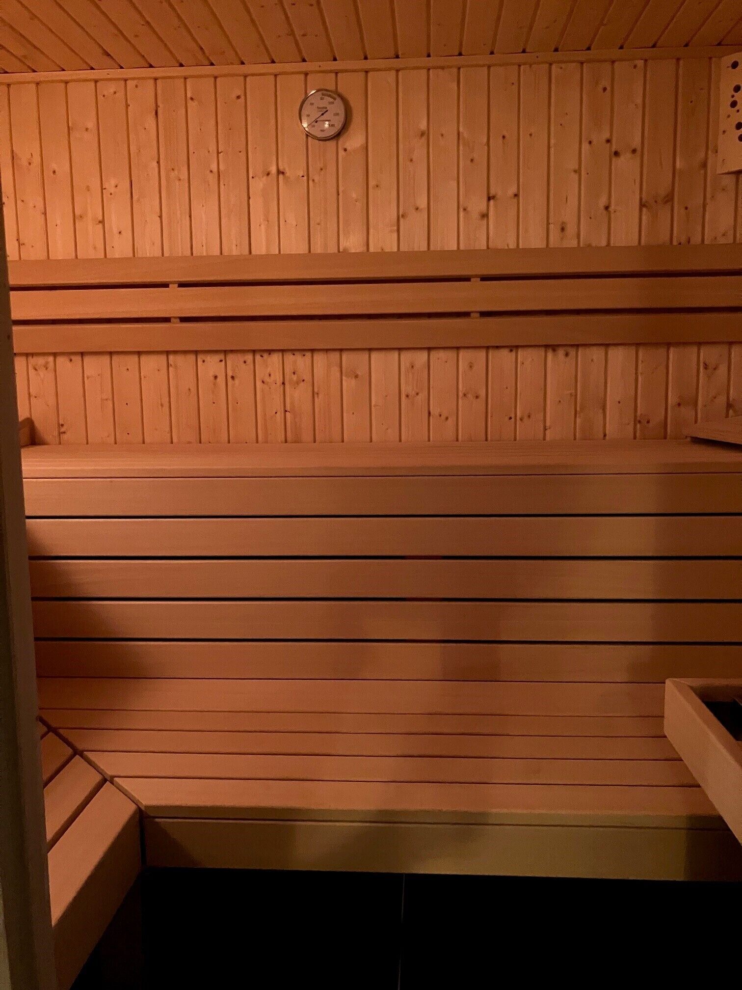Un sauna en bois, doté de bancs et d’un thermomètre fixé au mur.