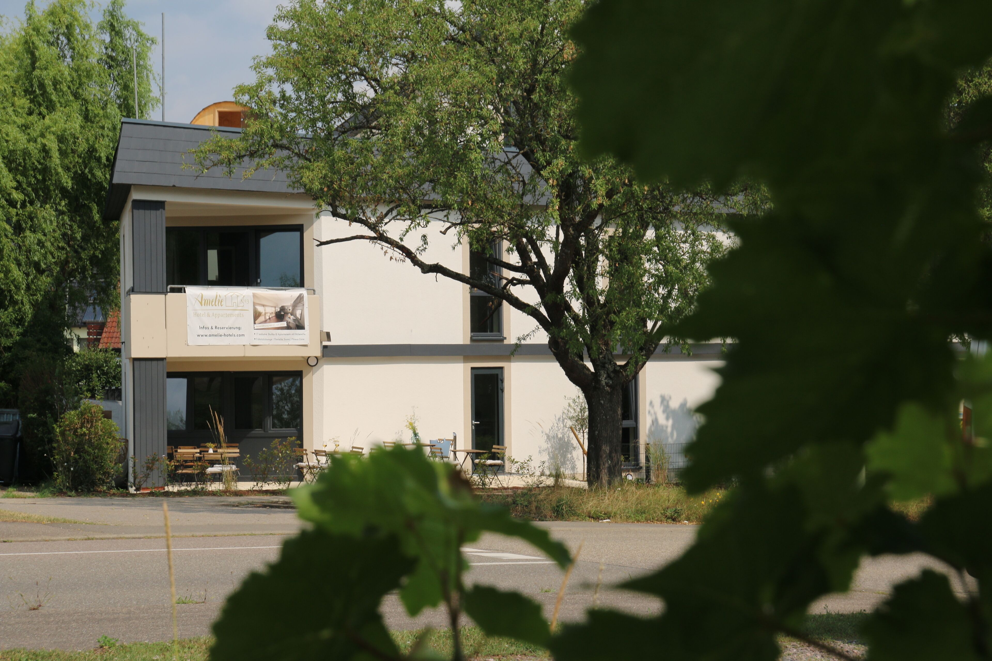 A two-story building with a balcony, a tree in front, and a signboard.
