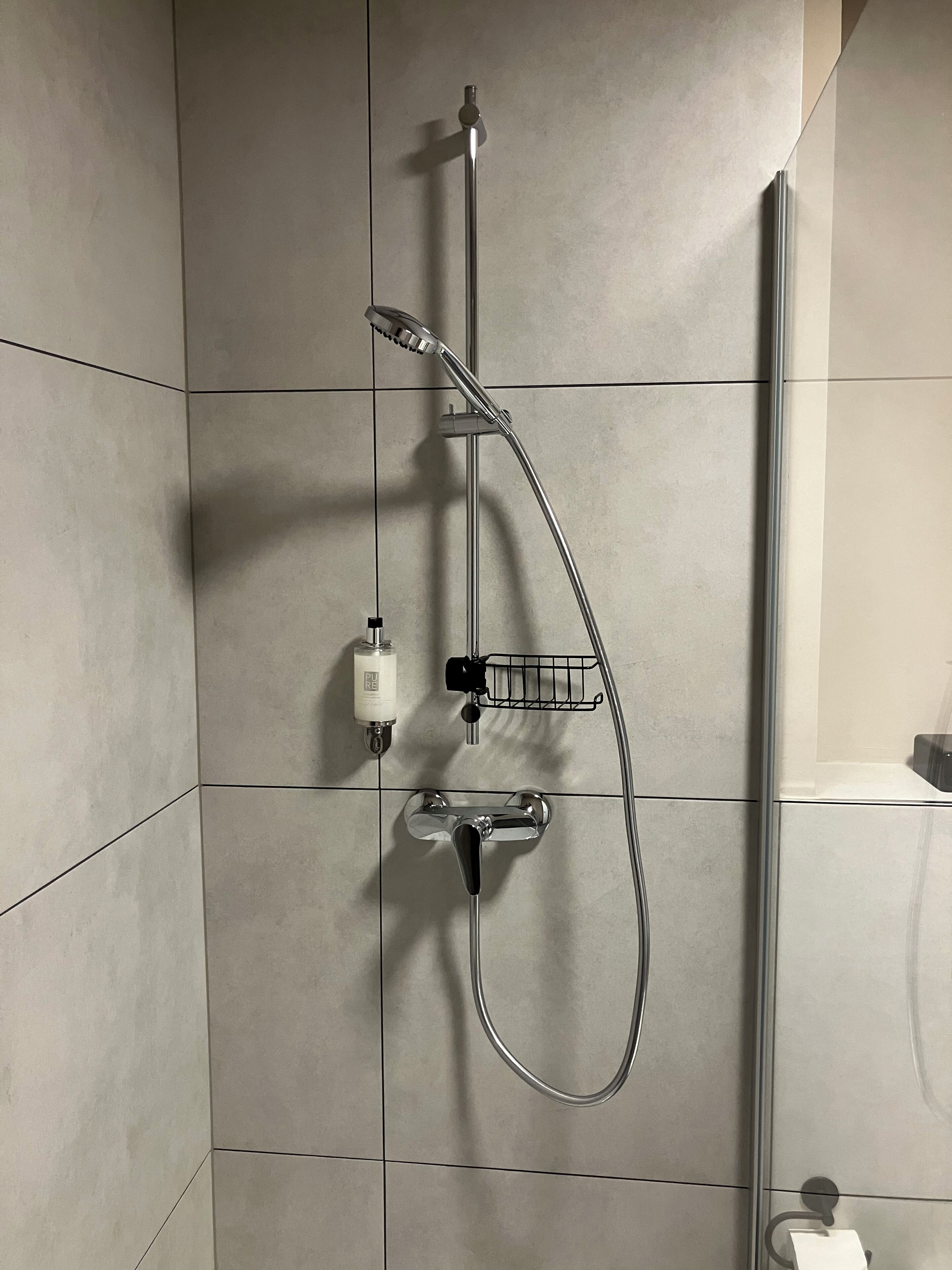 A shower with a handheld showerhead, a wall-mounted faucet, and a soap dispenser.