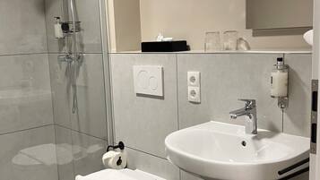 Une salle de bain moderne avec une douche à l’italienne en verre, des toilettes blanches, un lavabo avec un miroir au-dessus et un meuble noir en dessous.