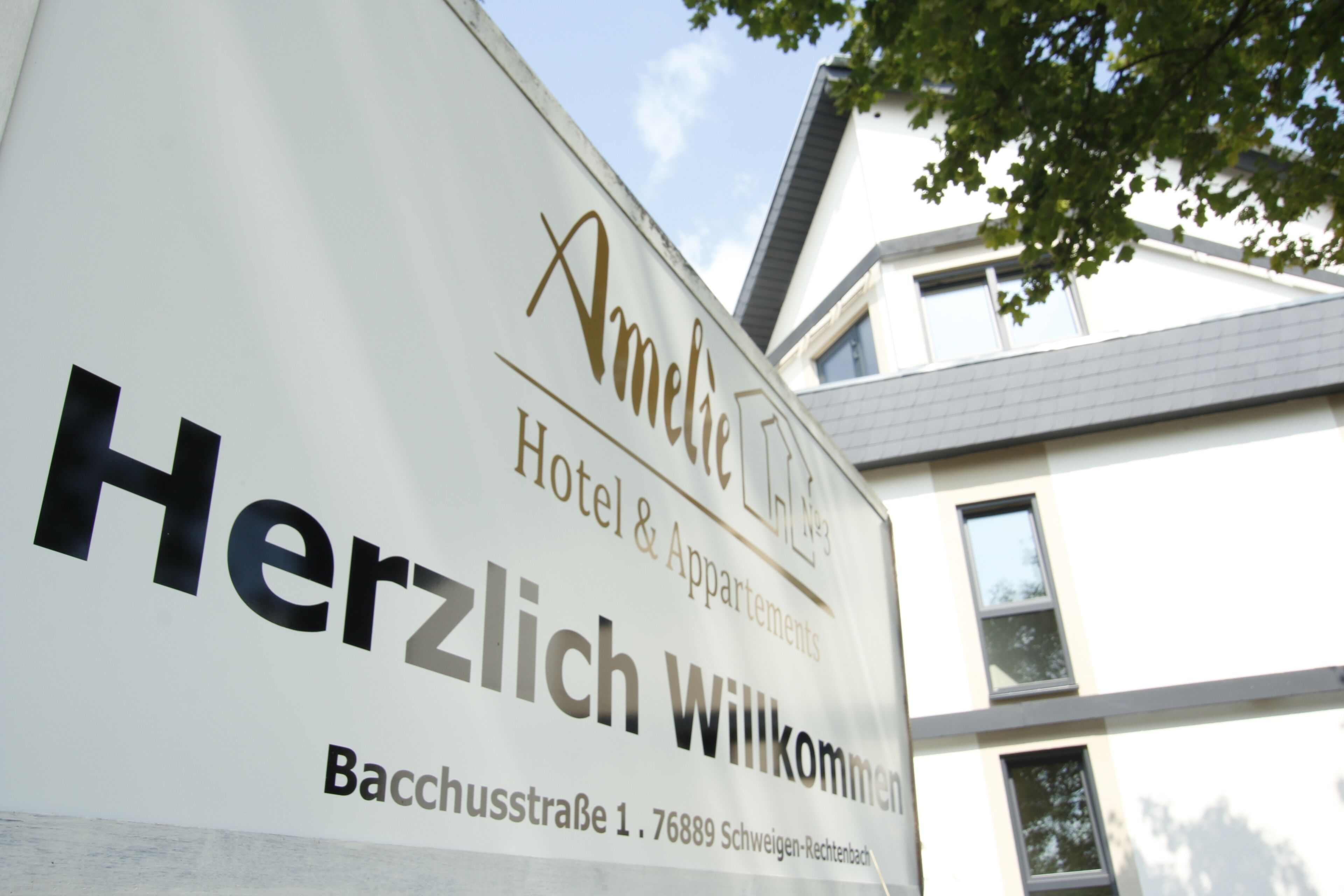 A hotel sign with the name "Amelie Hotel & Apartments" and the address "Bacchusstraße 1, 76889 Schweigen-Rechtenbach".