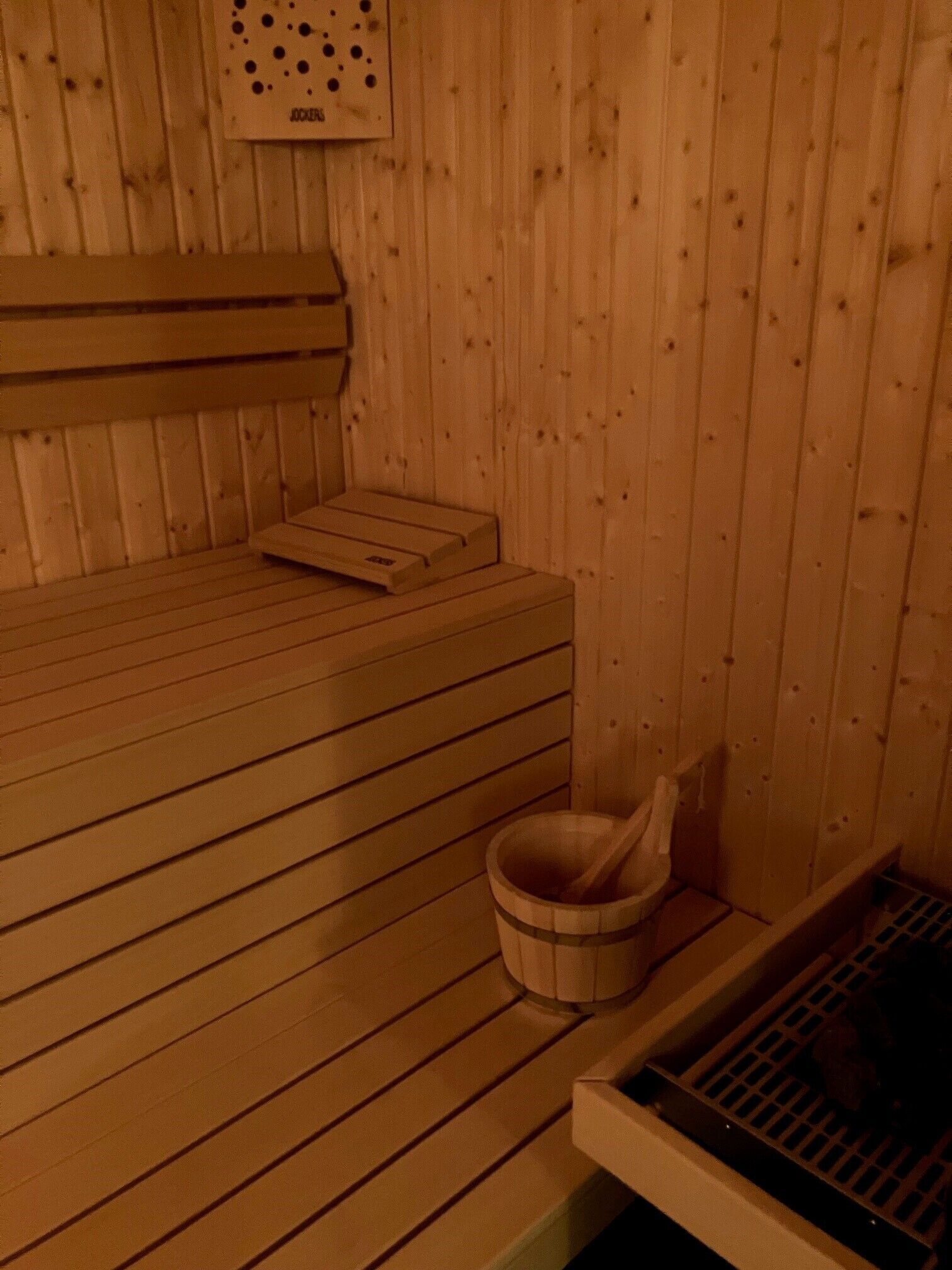 A sauna room with wooden benches, a wooden bucket, and a ventilation system.