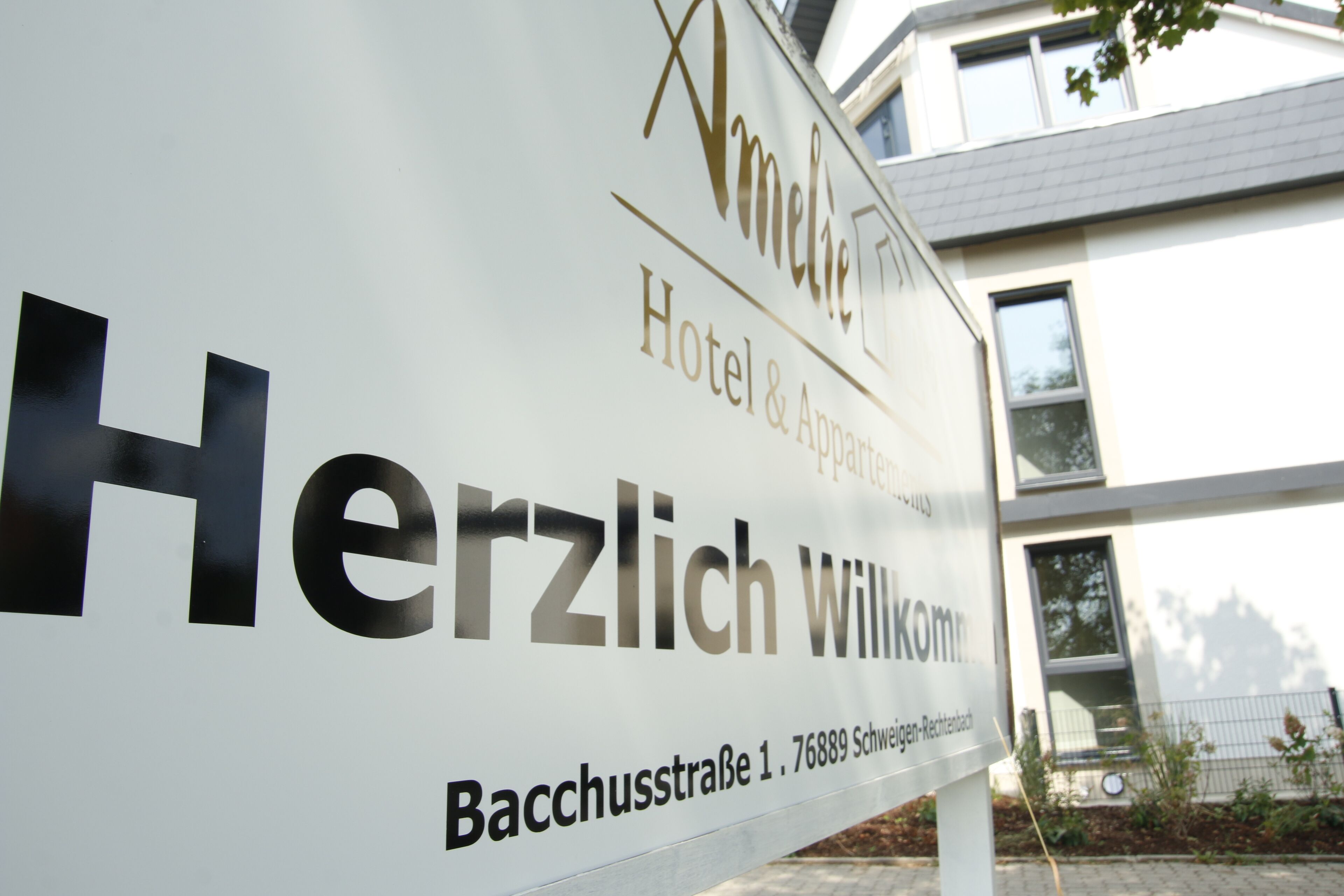 Schild mit der Aufschrift 'Herzlich Willkommen' vor dem 'Amelie Hotel & Apartment' mit der Adresse 'Bacchusstraße 1, 76889 Schwingen-Reutach'.