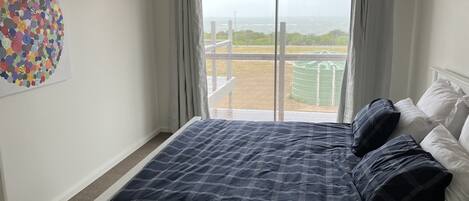 A bedroom with a large bed, a view of a green field through a sliding door, and a colorful abstract art piece on the wall.