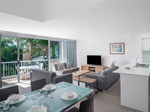 Sala de estar moderna com sofá, televisão, mesa de jantar e varanda com vista para o verde.