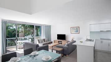A modern living room with a dining area, a kitchen, and a balcony with a view of greenery.