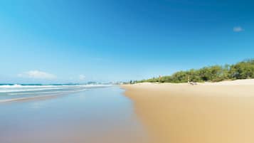 A beach with a clear sky, calm sea, and distant buildings.