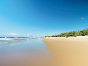 Una playa con cielo despejado, mar tranquilo y edificios a lo lejos.