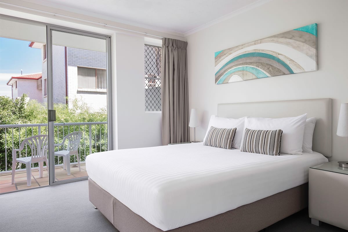 Ein Hotelzimmer mit einem großen Bett, einem Balkon mit Stühlen und Blick auf Gebäude.