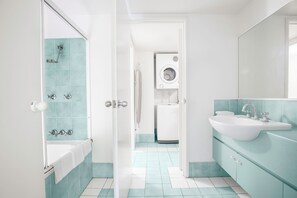 A bathroom with a bathtub, a sink, and a washing machine. - Breakfree Diamond Beach Broadbeach (Gold Coast)