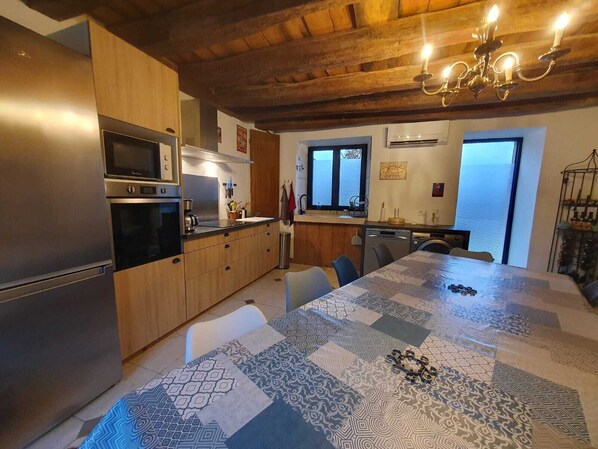 Une cuisine moderne avec des meubles en bois, des appareils électroménagers en acier inoxydable et une grande table à manger recouverte d’une nappe à motifs.