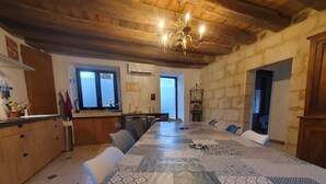 A spacious dining area with a long table, wooden ceiling beams, and a chandelier.
