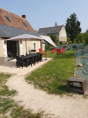 Une terrasse extérieure avec une table et des chaises, un espace salon couvert et un bâtiment en pierre en arrière-plan.