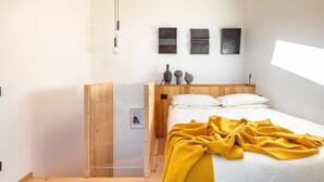 Ein modernes Schlafzimmer mit einem Holzschrank, einem Bett mit weißer Bettwäsche und einer gelben Decke sowie drei an der Wand befestigten Kunstwerken.