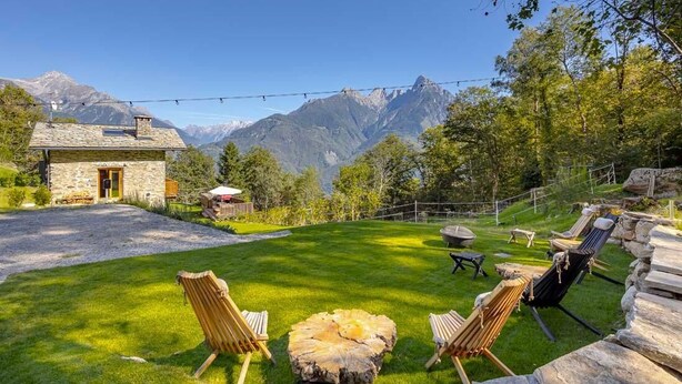 Ein Steinhaus mit einem Rasen, Sitzgelegenheiten im Freien und Blick auf die Berge.