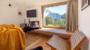 Ein Schlafzimmer mit großem Fenster, Holzmöbeln, einem Fernseher und Blick auf die Berge.
