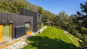 Ein modernes Haus mit einem Kiesweg, der zu einer Holztür führt, umgeben von einem gepflegten Rasen und Bäumen.