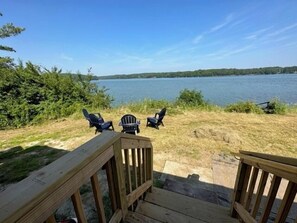 Una terraza de madera con tres sillas Adirondack mirando un lago.