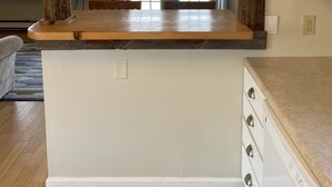 A kitchen with a wooden beam ceiling, a built-in island with a sink, and a view of a dining area with a window.