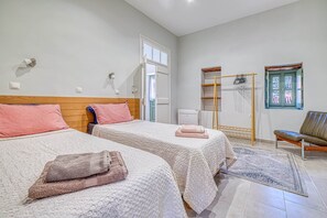 A hotel room with two beds, a wooden headboard, a window with a view, a bench, and a drying rack.