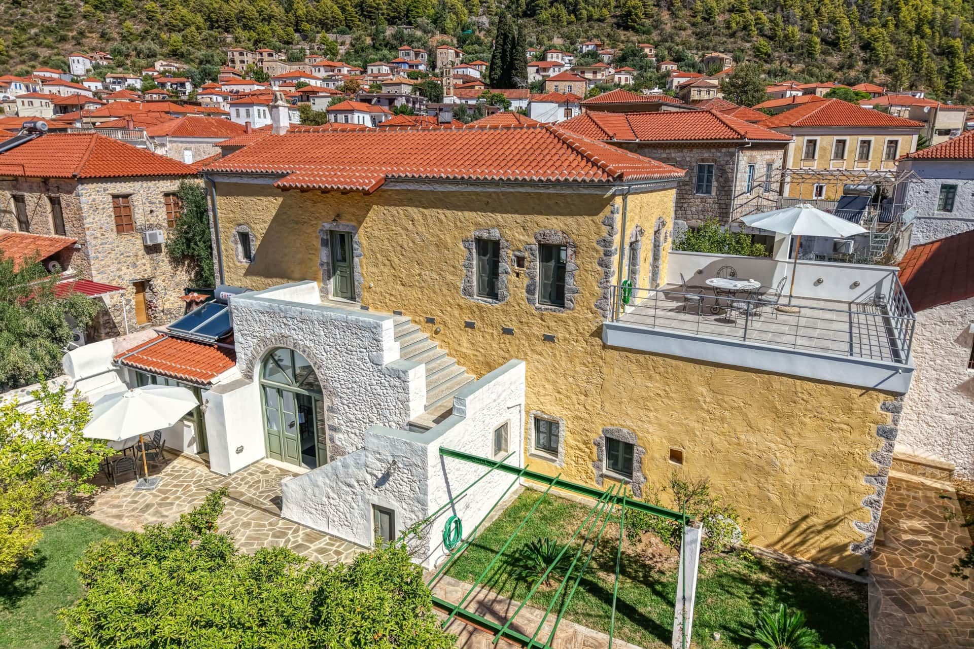 A residential area with stone buildings, red-tiled roofs, and a clear view of the surrounding hillside.