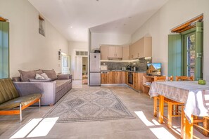 A compact living space with a kitchenette, a dining area, and a seating area with a sofa and a bench. - Alexander House Apartment 2 (Leonidi)