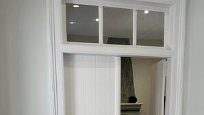 A narrow hallway leading to a bedroom with a bed, a nightstand, and a lamp.