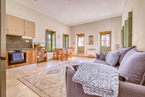 A spacious living area with a sofa, a dining table, and a kitchen with wooden cabinets and a built-in oven. - Alexander House Apartment 2 (Leonidi)