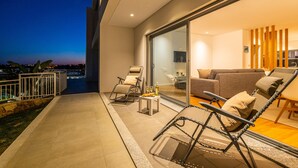 Een modern buitenverblijf met een glazen deur naar een woonkamer, ingericht met een bank, stoelen en een bijzettafeltje met drankjes.