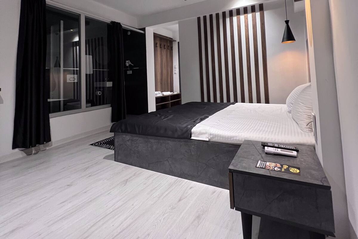 A modern bedroom with a large bed, a bedside table, a hanging lamp, and a window with curtains.