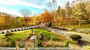 A landscaped garden with a pathway leading to a bench, surrounded by trees and a white fence.
